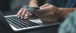 Nešiojamasis kompiuteris ir mokėjimo kortelė rankoje, atliekamas mokėjimas internetu kortele